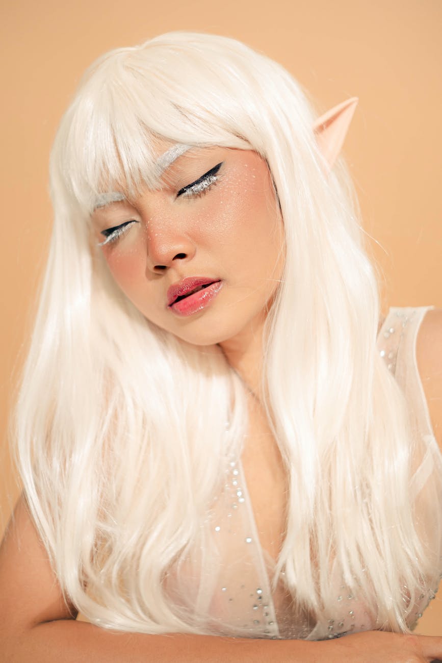 portrait of a pixie with white hair and closed eyes against beige background